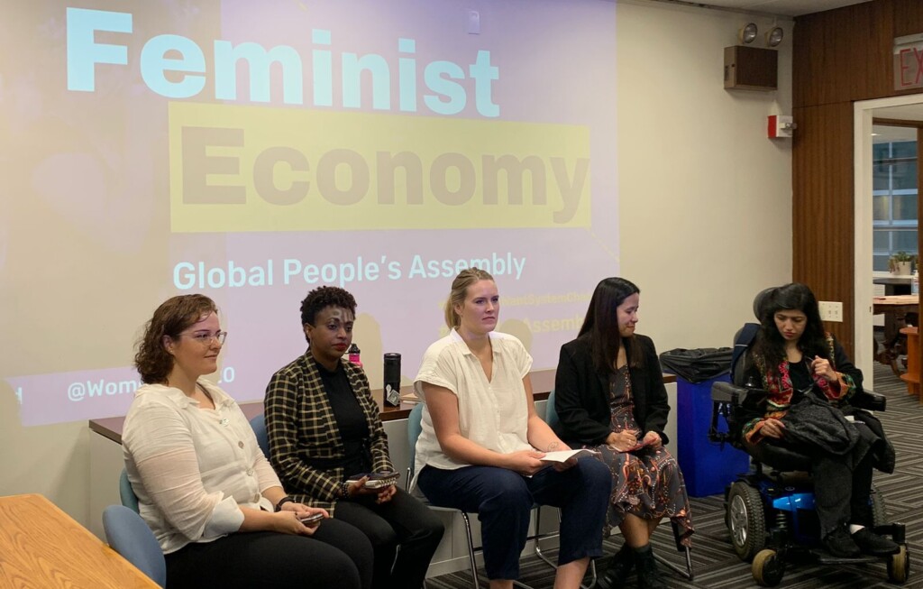 Image description: A diverse group of five feminist activists panel a session at the Global People's Assembly. Behind them, a projected screen reads - Feminist Economy.